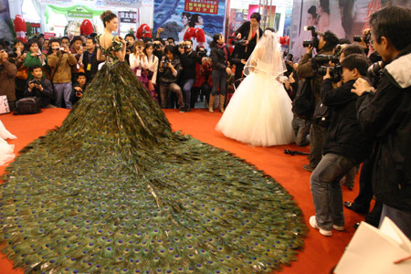 A model presents a wedding dress decorated with peacock feathers at the 