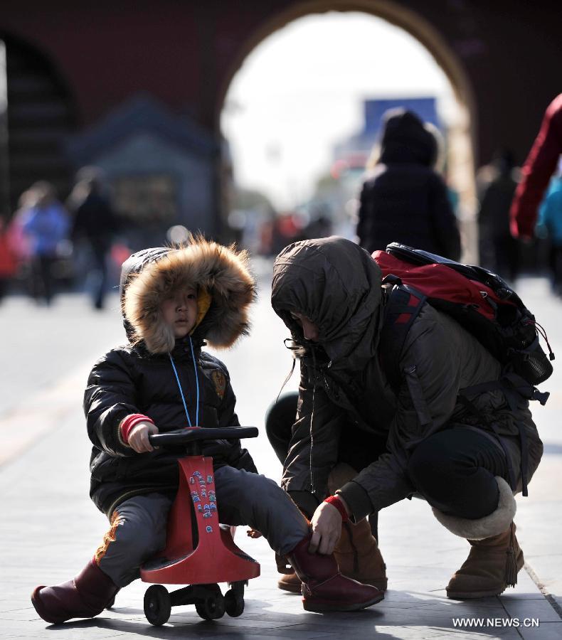 A woman helps a boy wear windproof boots at the Tiantan Park in Beijing, capital of China, Nov. 11, 2012. Beijing experienced windy weather and a sharp fall in temperature on Sunday following a rainfall the previous day. (Xinhua/Li Wen) 