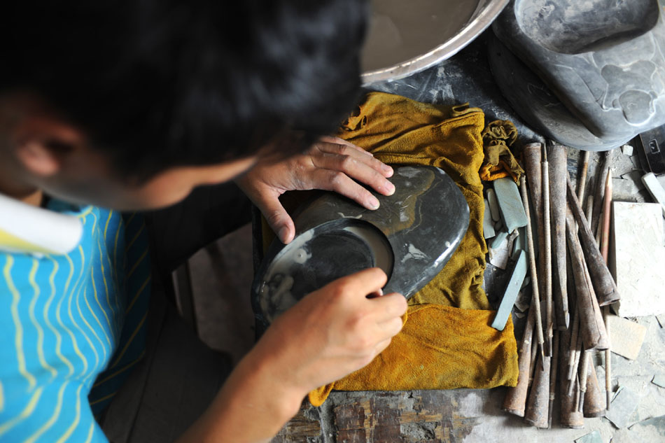 An apprentice of Wen Xin polishes an inkstone in Shexian County of east China's Anhui Province, Aug. 7, 2012. (Xinhua/Du Yu)