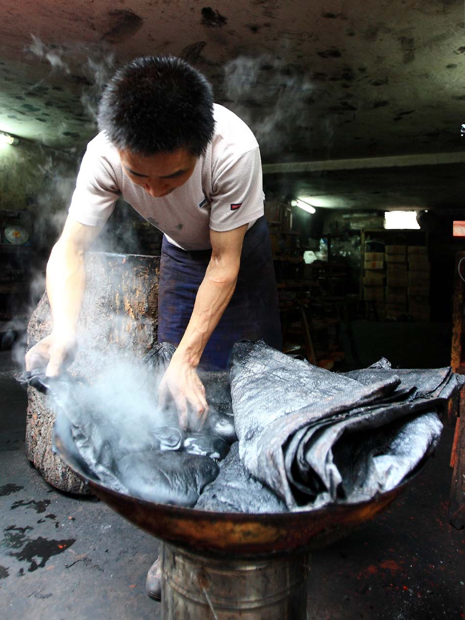 Huang Jun, a worker of Xiang Shengli's studio, picks up the raw material from a heating pot in Shexian County of east China's Anhui Province, Aug. 8, 2012. (Xinhua/Xu Zijian)