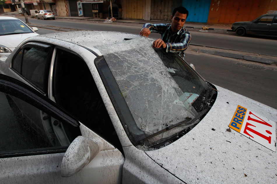 A Palestinian journalist inspects the damaged news car after air strikes in Gaza City, on Nov. 18, 2012. (Photo/Xinhua)