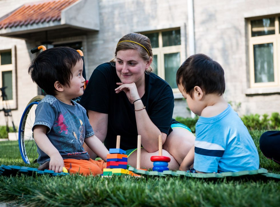 Taylor, an American voluntary worker, plays with two kids on the grass in the Shepherd's Field Children's Village at the Shepherd's Field in Tianjin, north China, May 28, 2012.(Xinhua/Zhang Chaoqun)