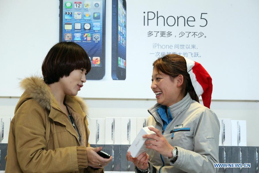 A salesperson (R) presents an iPhone 5 cell phone to be sold in Binhai New Area in Tianjin, north China, Dec. 13, 2012. Apple iPhone 5 is scheduled to be released in the Chinese mainland on Friday. (Xinhua)
