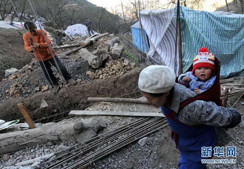 An old man carrying a child walks past the self-built buildings in earthquake-stricken area in Yiliang, Yunnan on Dec. 13, 2012. The earthquake (MS 5.7) that jolted Yiliang in Yunnan on Sept. 7, 2012 damaged most houses there. Local government said house reconstruction is the most important assignment and repairing and reinforcing work must be completed before the Spring Festival in 2013. (Xinhua/Lin Yiguang)