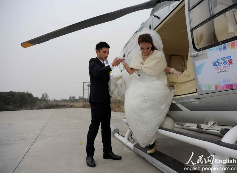 A groom helps his bride down from a helicopter on their wedding day in Ningbo, East China's Zhejiang province on Jan 16, 2013. The newlyweds paid over 20,000 yuan per hour to rent the 60 million yuan helicopter.(Photo/People's Daily Online)