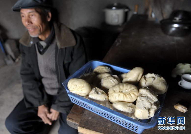 Wang Yizhong, a farmer, sits beside the table on which is a basket of his one-week grain ration, in Longnan, Gansu on Jan. 20. He said monthly income of him and his wife is 200 yuan in total, so they are unable to afford meats for meal and have never been to restaurants. (Photo/Xinhua)