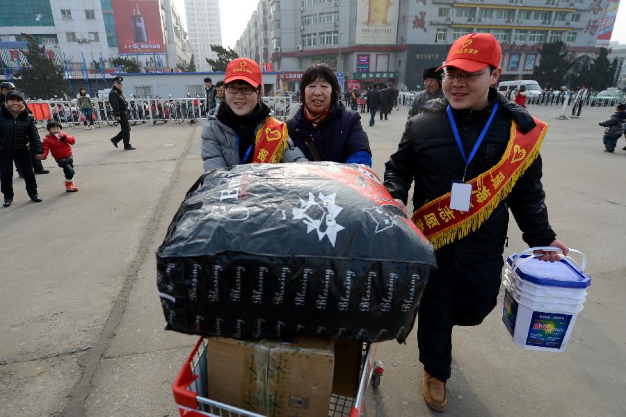 Volunteers help a passenger (C) to carry her luggage at Hefei Train station in Hefei, capital of east China's Anhui Province, Jan. 23, 2013. A total of 100 volunteers began their work at Hefei train station to help the passengers in the Spring Festival travel peak. (Xinhua/Zhang Duan) 