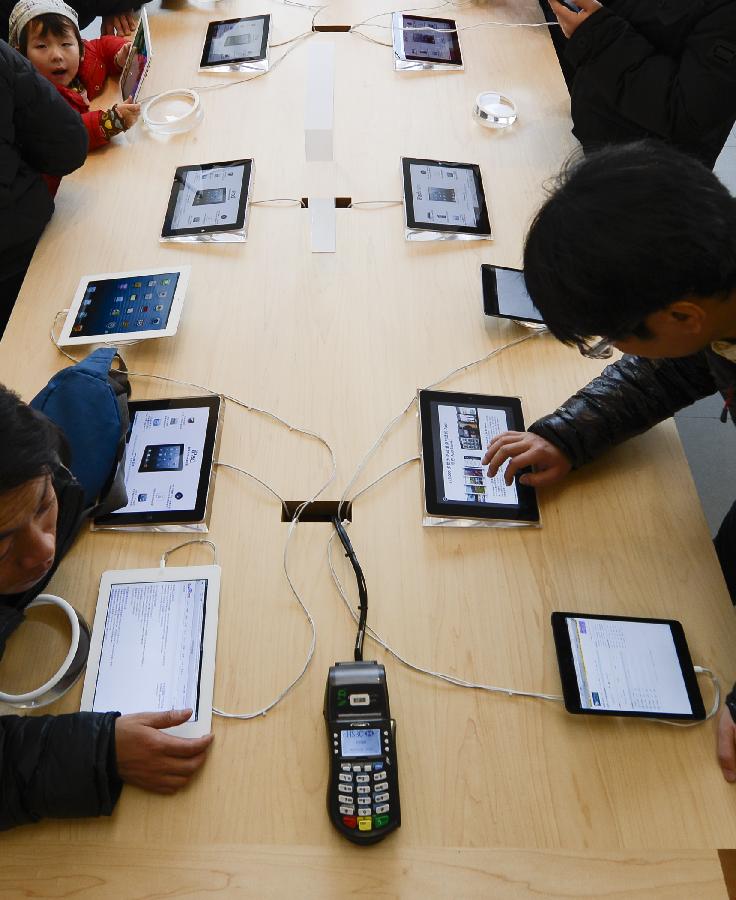 Customers play ipads at Wangfujin Apple Store in Beijing, capital of China, Jan. 25, 2013. Apple Store held a sales activity on Friday, during which customers could enjoy special pricing online and at Apple retail stores on apple products. (Xinhua/Qi Heng)