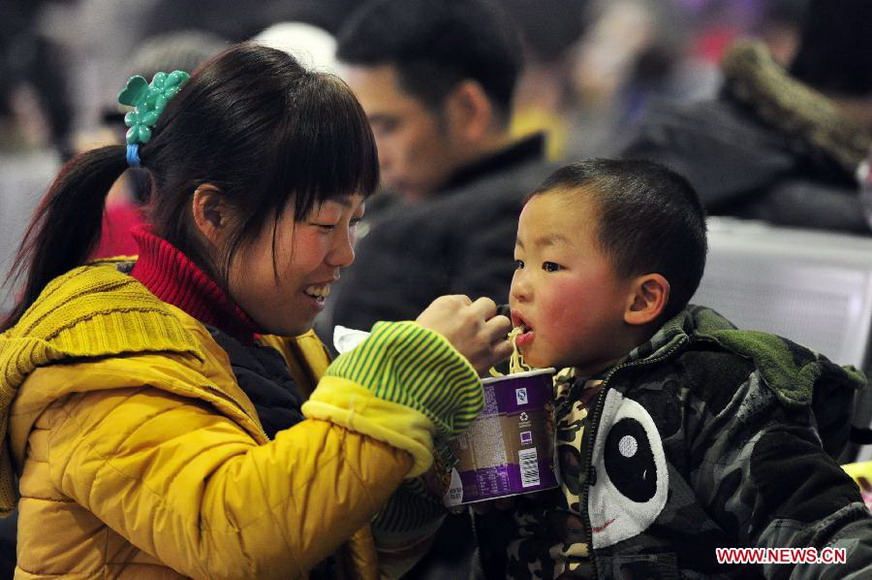 A woman feeds instant noodles to her child at the waiting hall of railway station in Ji'nan, capital of east China's Shandong Province, Jan. 26, 2013. The 40-day Spring Festival travel rush started Saturday. (Xinhua/Cui Jian)