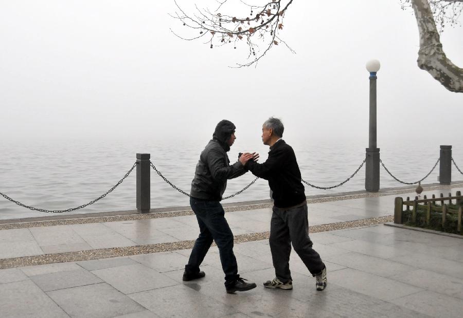 Citizens do morning exercises amid heavy fog on a bank of the West Lake in Hangzhou, capital of east China's Zhejiang Province, Jan. 28, 2013. The provincial meteorological observatory has issued an orange-coded alert on Jan. 28 morning as foggy weather here cut visibility to less than 500 meters and worsened air pollution in many cities. (Xinhua/Yue Deliang) 