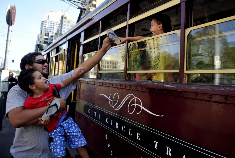 Passengers try to hand over a slipper from a tram in Melbourne, Australia, Jan. 28, 2013. Melbourne's trams network is one of the largest functioning tram networks in the world. Among all the routes, No. 35, the City Circle Tram provides a free and convenient way for visitors to see the sights of central Melbourne while experiencing a ride on one of the city's much loved heritage trams. (Xinhua/Chen Xiaowei) 