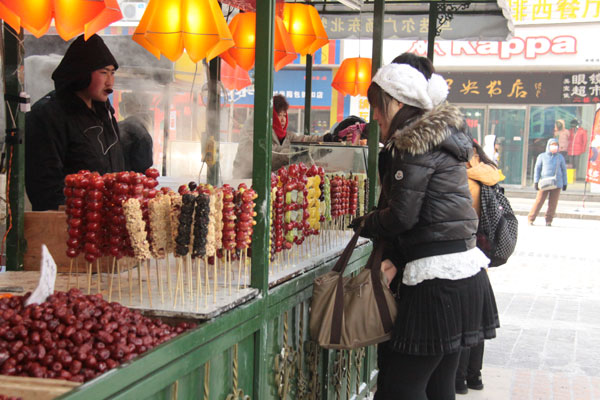 Two customers buy "tanghulu" (crispy, sugar-coated fruit on a stick) on Central Street in Harbin, northeast China's Heilongjiang Province, on December 17, 2012. [Photo: CRIENGLISH.com] 
