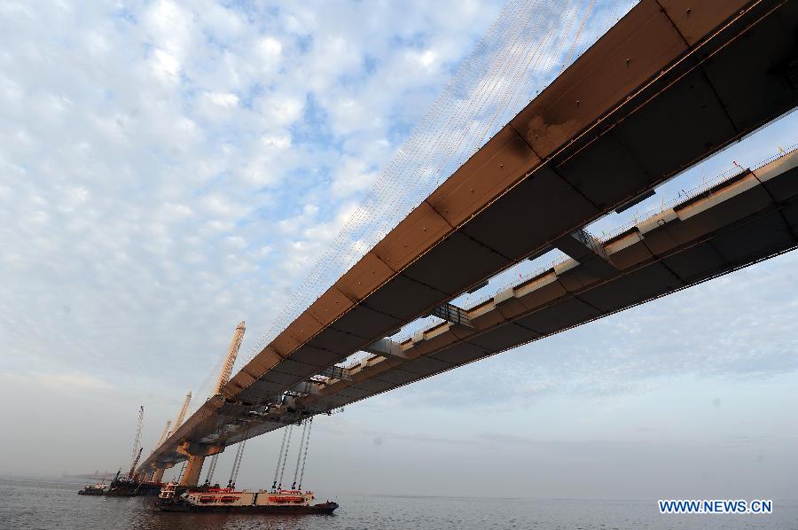 Photo taken on Feb. 3, 2013 shows boats carrying the last two steel box girders, each of which weighs 408 tons, anchor below the joint of the main span of the Jiaxing-Shaoxing Sea-Crossing Bridge in Shaoxing, east China's Zhejiang Province. The Jiaxing-Shaoxing Sea-Crossing Bridge, the 2nd sea-crossing bridge in Zhejiang , will be the world's longest and widest multi pylon cable-stayed bridge when it is finished. It is expected to halve the driving time from Shaoxing to Shanghai in east China after putting into use in June of 2013. (Xinhua/Xu Yu)