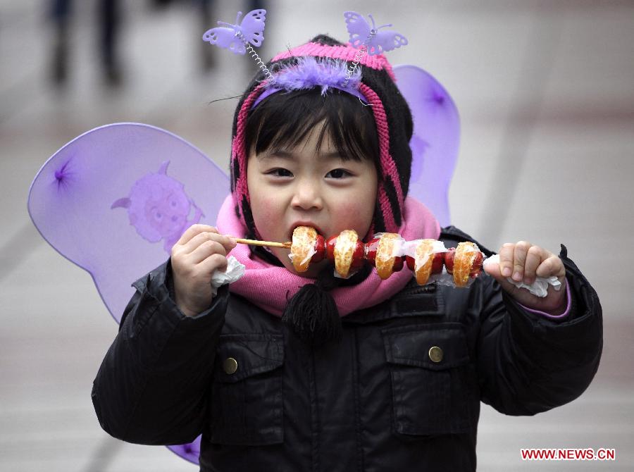 A child tastes a sugarcoated haws on a stick at a temple fair in Nanjing, capital of east China's Jiangsu Province, Feb. 11, 2013. Temple fair, a Chinese cultural gathering traditionally adjacent to temples, is usually held around the time of the Chinese Lunar New Year. At the fair, activities include worshiping deities, entertainment and shopping. (Xinhua/Li Wenbao)