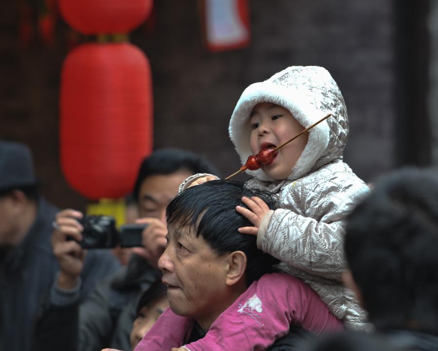 A young girl tastes sugarcoated haws while sitting on the shoulder of her father on a street of the Ciqikou Town in southwest China's Chongqing Municipality, Feb. 13, 2013. Large amount of tourists visited the time-honored Ciqikou during the Spring Festival holiday. (Xinhua/Liu Chan) 