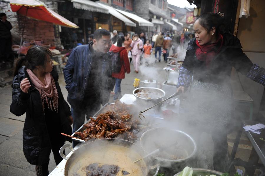 Tourists stop at a vender's stall on the street of Qingyan Town in Guiyang, capital of southwest China's Guizhou Province, Feb. 13, 2013. Large amount of tourists visited the time-honored Qingyan Town during the Spring Festival holiday. (Xinhua/Ou Dongqu) 