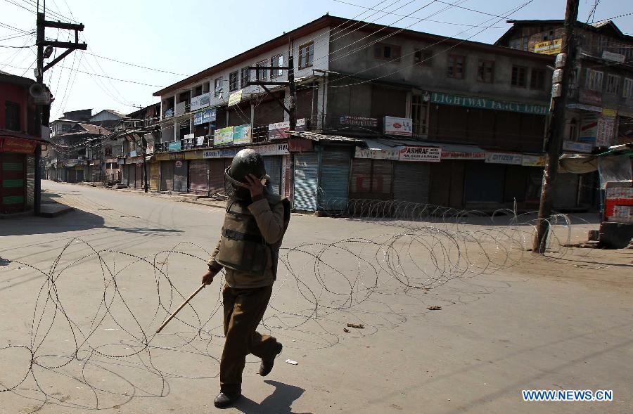 An Indian policeman adjusts his cap as he walks past barbed wire during curfew in Srinagar, summer capital of Indian-controlled Kashmir, March 6, 2013. Indian army troopers on Tuesday killed a young man and wounded another after opening gunfire at protesters in Indian-controlled Kashmir, officials said. (Xinhua/Javed Dar) 