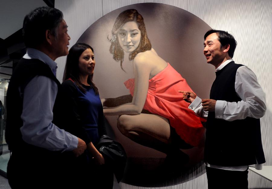 Artist Hou Qing (R) introduces his work to visitors during his painting exhibition in Hong Kong, south China, March 7, 2013. The 12-day painting exhibition would show 15 paintings of modern women created by artist Hou Qing since Thursday. (Xinhua/Chen Xiaowei) 
