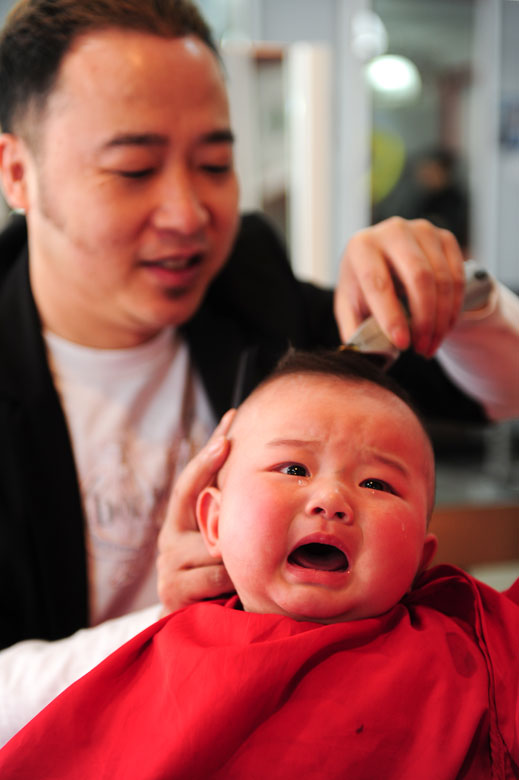 A barber cuts hair for a five-month-old baby in Yantai, Shandong province, March 13, 2013. In Chinese traditional custom, people cut hair for good luck on  second day of second lunar month, or “Er Yue Er” in Chinese, which lied on the last Wednesday. (Xinhua/Chu Yang)