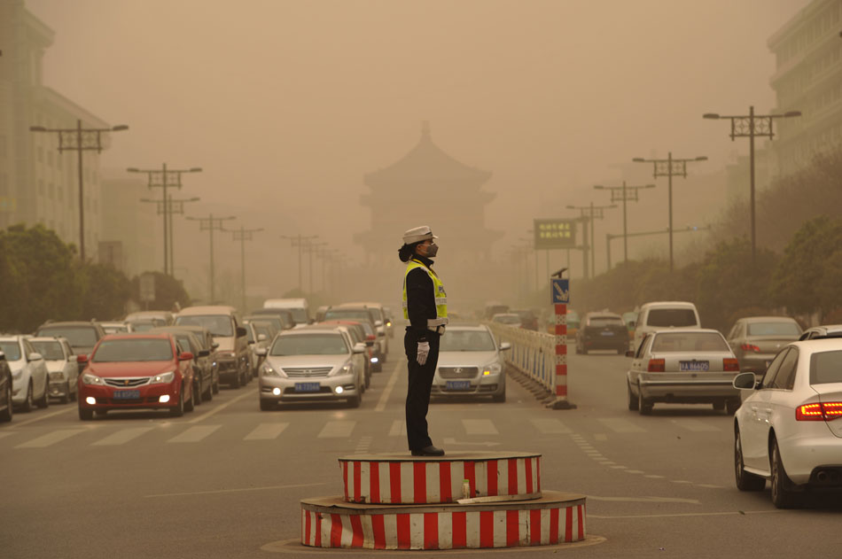 A mask-wearing female police officer directs the traffic in heavy sand and dust blown by a new round of cold front, Xi’an, northwest China’s Shaanxi province,  March 9, 2013. (Xinhua/Ding Haitao)