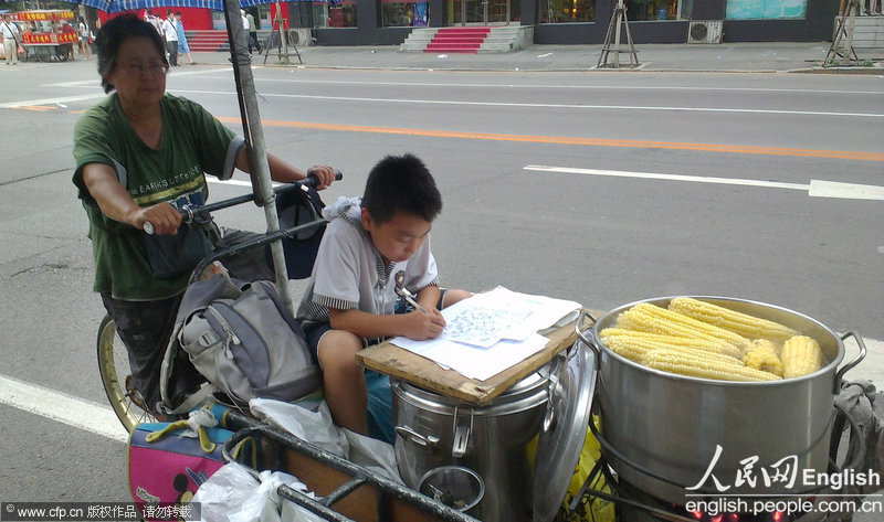A boy does his homework on the snack wagon drove by his grandmother in Shenyang, Liaoning province. (Photo by Luo Lan/ CFP)