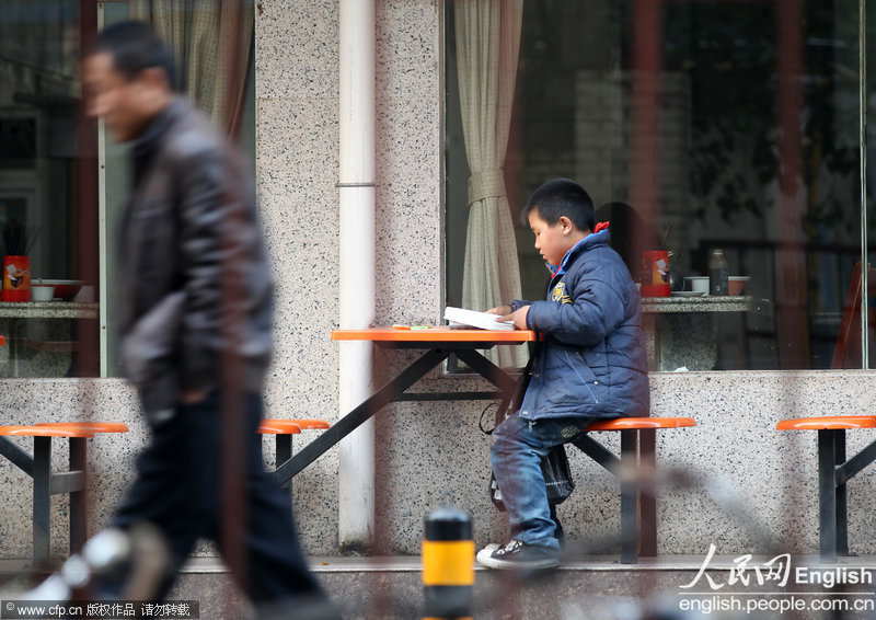 A 10-year-old boy does his homework at the roadside in Zhengzhou, Henan province. (Photo by Hou Jianxun/ CFP)