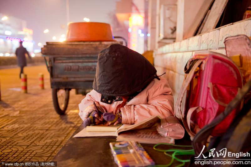 A little girl does her homework in the dim light of a street lamp in Pingdingshan, Henan province. (Photo by Xiao Jian/ CFP)