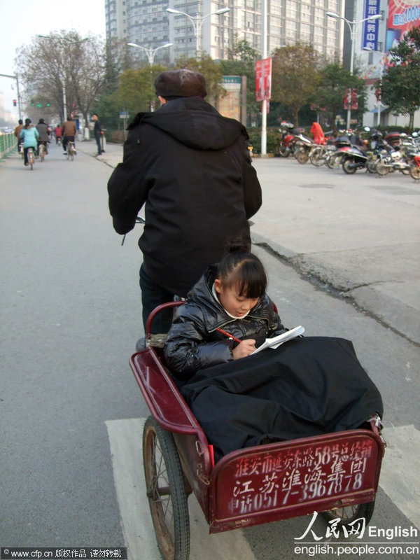 A little girl sitting in the tricycle does her homework as her grandfather rides the tricycle to go to work in Xuzhou, east China’s Jiangsu province.(Photo/ CFP) 