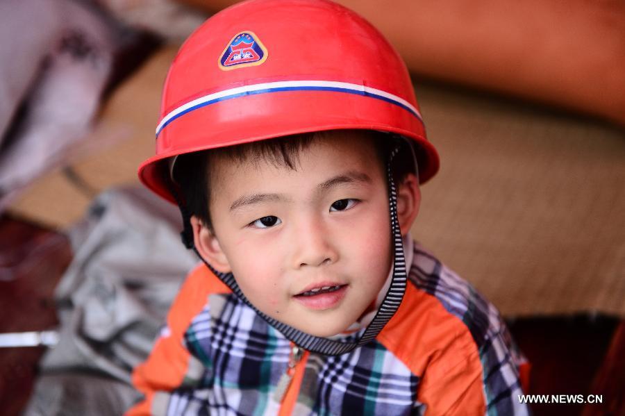 Four-year-old boy Hu Hanwei wears a helmet sitting inside a tent in the quake-hit Lushan County, southwest China's Sichuan Province, April 21, 2013. (Xinhua/Zhang Hongxiang) 