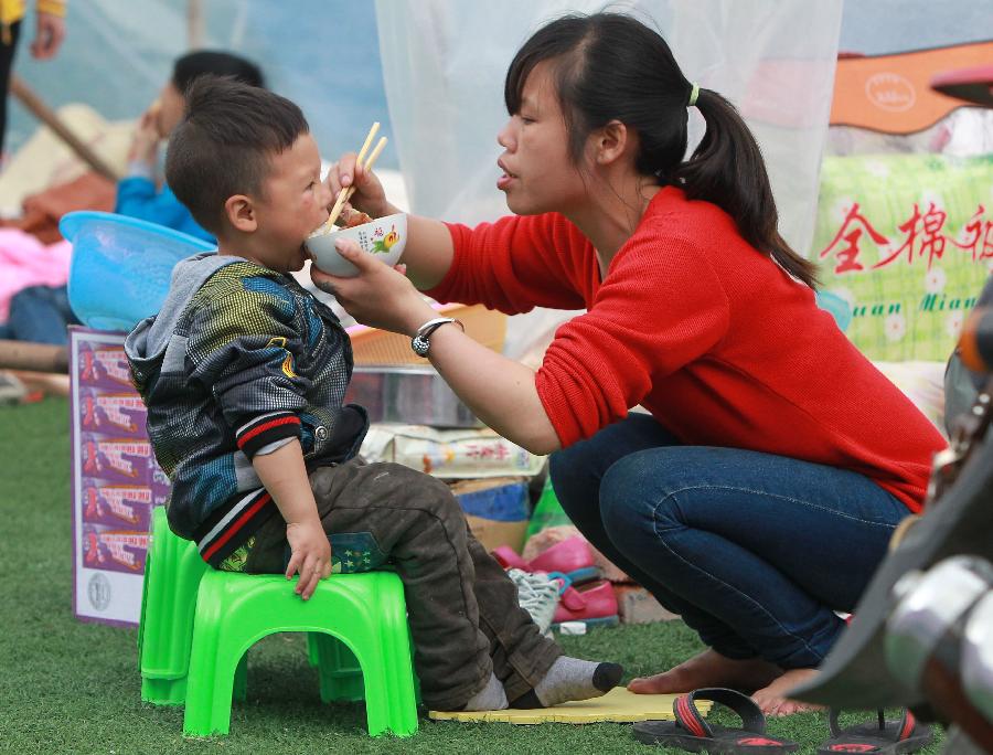 A woman feeds her son outside a tent at a temporary settlement in the quake-hit Baoxing County, southwest China's Sichuan Province, April 22, 2013. (Xinhua/Pei Xin)