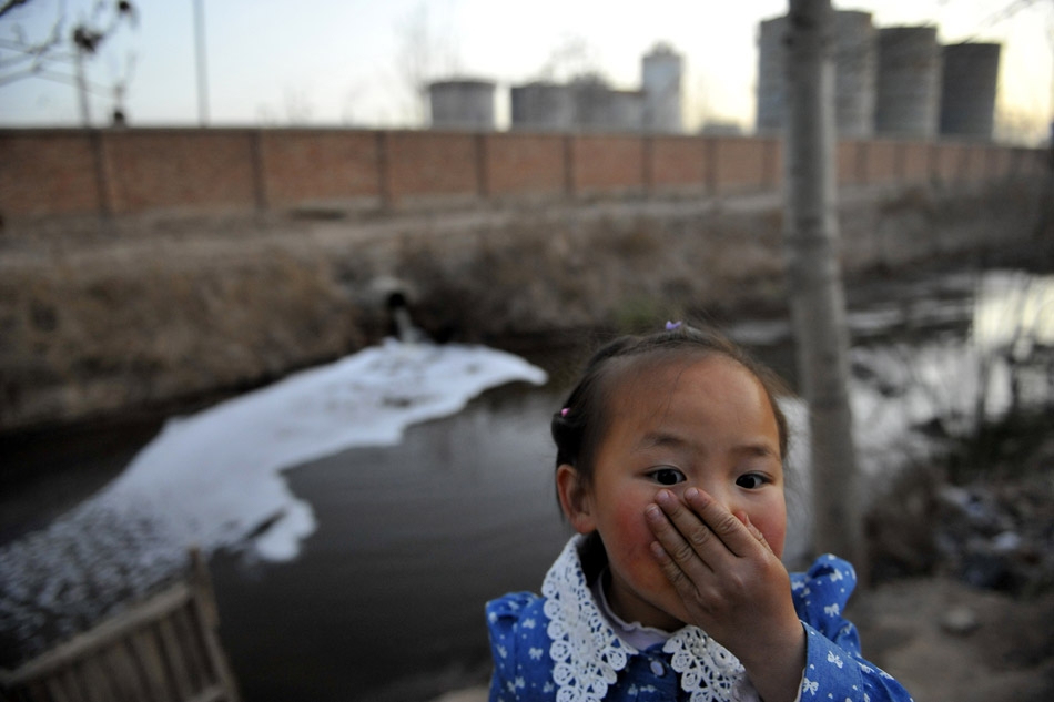 A girl covers her nose near the outfall of the Ningxia Terry Pharmaceutical Co., Ltd in Xingqing District of Yinchuan, Ningxia Hui Autonomous Region on April 1, 2013. Three big bio-fermentation pharmaceutical companies are located in the suburbs of Yinchuan. The production pollution caused serious impact on the air quality and agricultural production of the surrounding areas. People have called on the authorities to solve the pollution problems for years, but they have not been resolved. (Xinhua/Wang Peng)