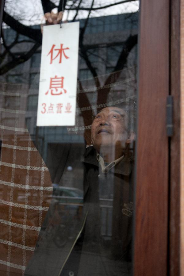 Zhang Guangyi attaches a wooden board with the Chinese characters meaning "shop closes and the shop opens at 3:00 p.m. " before leaving his shop after work in Beijing, capital of China, April 26, 2013. (Xinhua/Xu Zijian)