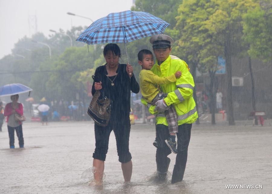 A traffic policeman carries a young boy to walk on the waterlogged road in Jiujiang City, east China's Jiangxi Province, May 15, 2013. A heavy rainfall hit the city on Wednesday. (Xinhua/Shen Junfeng)