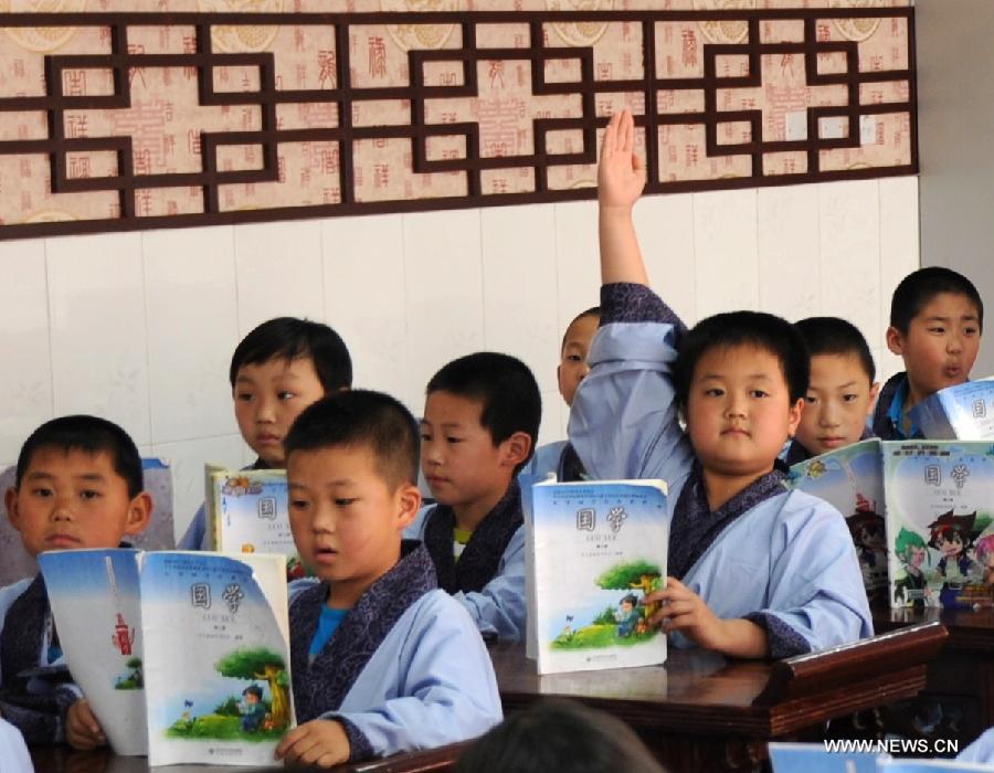 A boy raises his right hand to answer a question on a Chinese classics class at Shuangqiao Primary School in Pingquan County, north China's Hebei Province, June 14, 2013. Learning Chinese classics, like the Three-Character Classic and the Analects of Confucius, for one class hour per week has been part of the curriculum for students in Shuangqiao Primary School since 2009. (Xinhua/Wang Xiao)