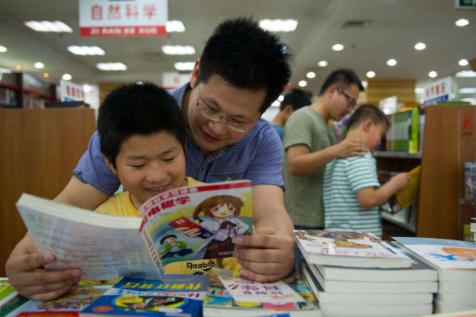 Xu Yu (L) reads a book for his “son” Zhang Tianyi in the Xinhua book store in Hefei, capital of Anhui province on June 15, 2013.  Officials of the Civil Affairs Bureau become one-day fathers, spending a weekend with orphans in Shushan District. (Photo by Du Yu/ Xinhua)