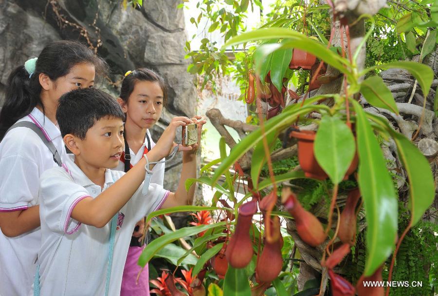 Students from Huiwen No.1 primary school take pictures of common nepenthes when visiting a greenhouse in the botanic garden in Beijing, capital of China, June 25, 2013. Students from a biology group of the Huiwen No.1 primary school visited Beijing Botanic Garden Tuesday to enrich their understanding of various plants. (Xinhua/Chen Yehua)