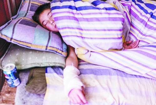 A 15-year-old boy falls asleep after the night shift in a restaurant's dormitory in Xi'an. His arm was wrapped in gauze because of scald caused by working. (Photo/China Youth Daily)