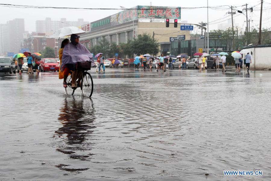 People are seen in rain on the flooded Guangcai Road in the Fengtai District of Beijing, capital of China, July 8, 2013. Beijing was hit by a thunder storm Monday morning. Rainfall is expected to continue in the next three days, according to the local meteorological authority. (Xinhua/Wang Yueling)