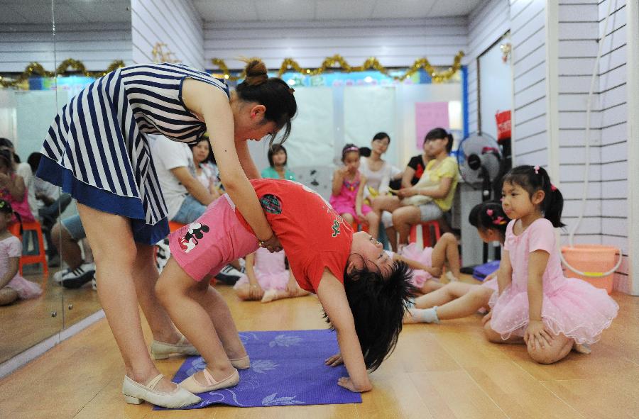 A teacher helps a young girl to do physical training at a dance class during the summer vacation in Shanghai, east China, July 7, 2013. (Xinhua/Lai Xinlin)