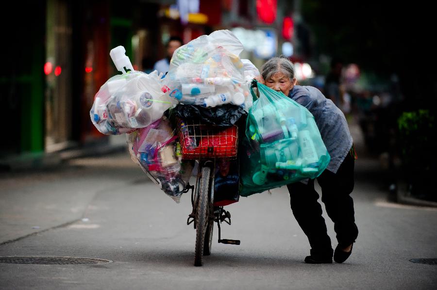 An old woman pushes a bicycle loaded with waste products heading for a waste recycling station on Shungeng Road in Jinan, capital of east China's Shandong Province, July 9, 2013. The 77-year-old woman makes a living by collecting and selling waste products. (Xinhua/Guo Xulei)