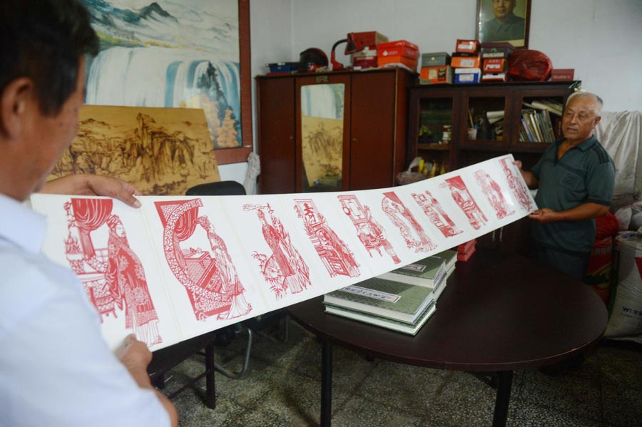 Li Xiangkui(R), 65, displays his paper-cut work of characters from "Dream of Red Mansions" in Cangzhou, Hebei province, July 7, 2013. (Photo/Xinhua)