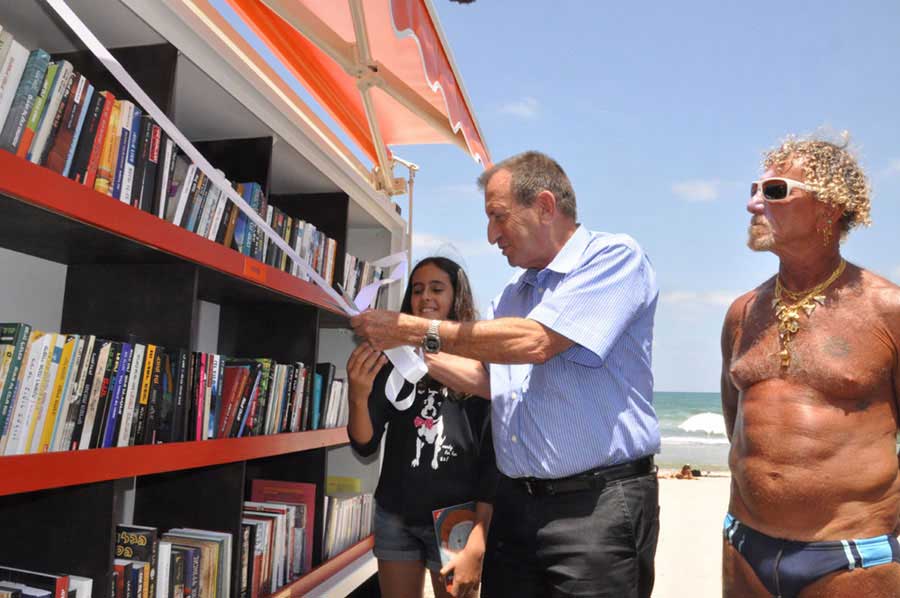 Tel Aviv-Yafo Mayor Ron Huldai (C) cuts the ribbon at the opening of a beach library with a girl and a lifeguard in Tel Aviv-Yafo on Tuesday, July 9, 2013. [Photo: CRIENGLISH.com / Zhang Jin]   