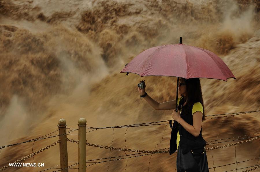 A tourist takes photos of the Hukou Waterfall of the Yellow River from the site in Jixian County, north China's Shanxi Province, July 12, 2013. Triggered by non-stop heavy rainfall in the upper reaches, the rising water level of the Yellow River surged the Hukou Waterfall, attracting many visitors. (Xinhua/Lu Guiming)