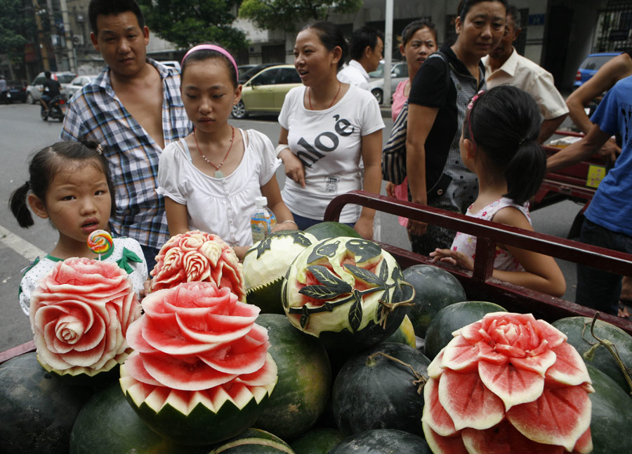 Customers are attracted by artistic watermelons in Xiangyang, Hubei province, on Monday, July 23, 2013. Zhang Yunxiao, a 30-year-old fruit dealer, carves vivid flowers like peonies and roses as well as other patterns on the melons. The price for each melon is 20 yuan ($3.26) to 50 yuan. (Photo / China Daily)