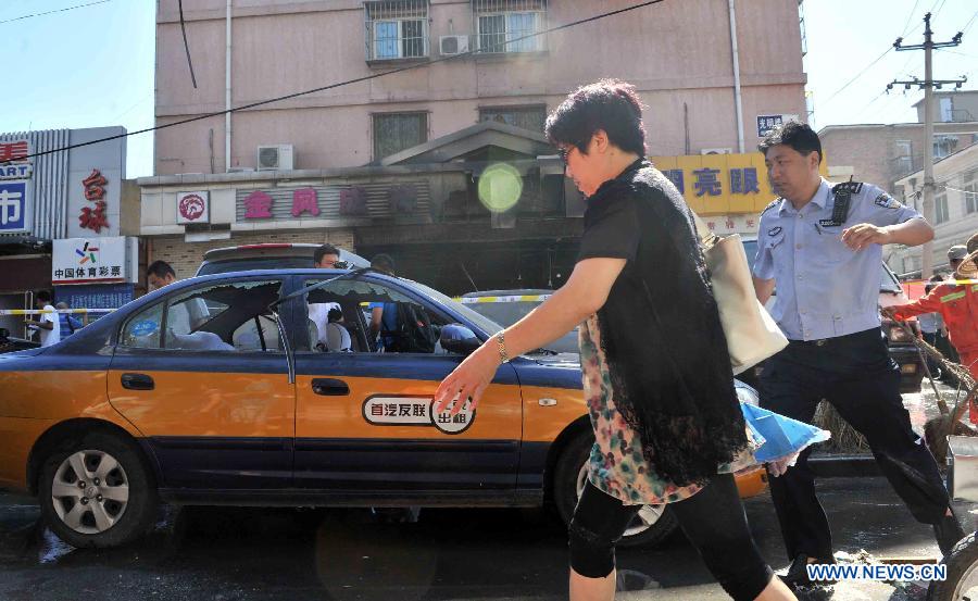 People walk past a taxi whose window glass was broken in an explosion at a cake shop on Guangming Road in Beijing, capital of China, July 24, 2013. A gas blast ripped through the cake shop Wednesday morning, leaving a number of people injured and vehicles damaged. (Xinhua/Li Wen)