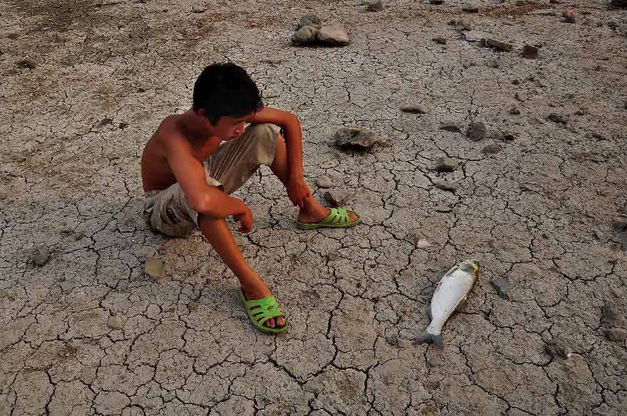 A boy sits on the chapped riverbeds near the Wantou Bridge over Yaojiang River in Ningbo, east China's Zhejiang Province, July 28, 2013. Unrelenting heat in Ningbo has drawn the water table of the Yaojiang River down and parts of the beds were chapped, which led to the death of mussels and fish. (Xinhua/Hu Xuejun)
